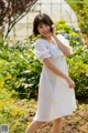 A woman in a white polka dot dress standing in a garden.