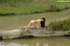 A naked woman sitting on a log in the water.