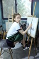 A young woman sitting on a chair painting on an easel.