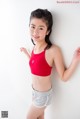 A young girl in a red sports bra top and gray shorts.