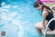 A woman in a blue swimsuit sitting on the edge of a swimming pool.