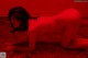 A naked woman laying on a bed in a red room.